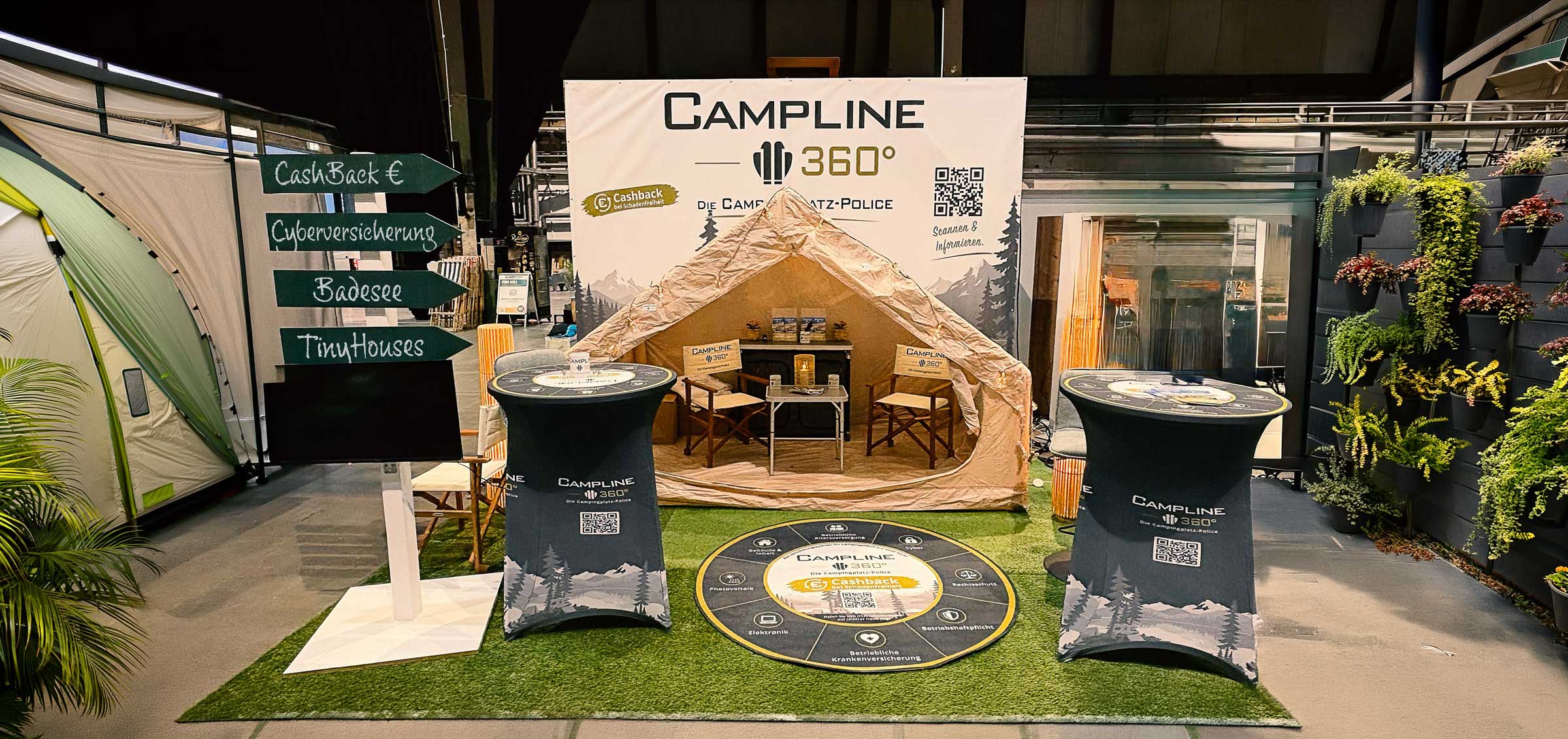 Messestand von Campline 360° mit Zelt, Sitzmöbeln, Stehtischen und Hinweisschildern zu Campingversicherungen.