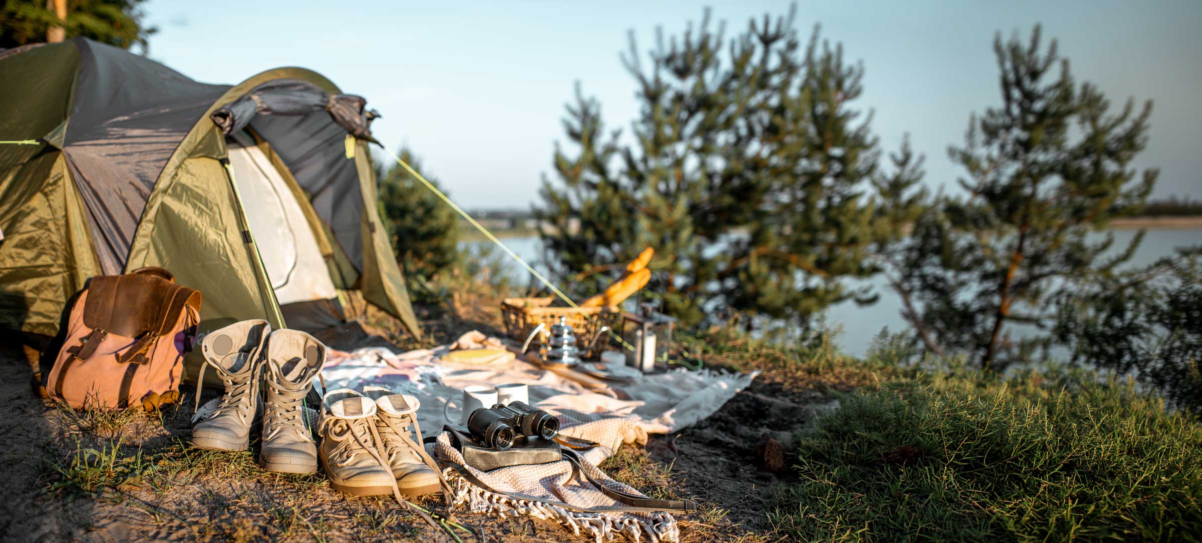 Ein Zelt mit Rucksack, Wanderschuhen und Fernglas an einem Seeufer.